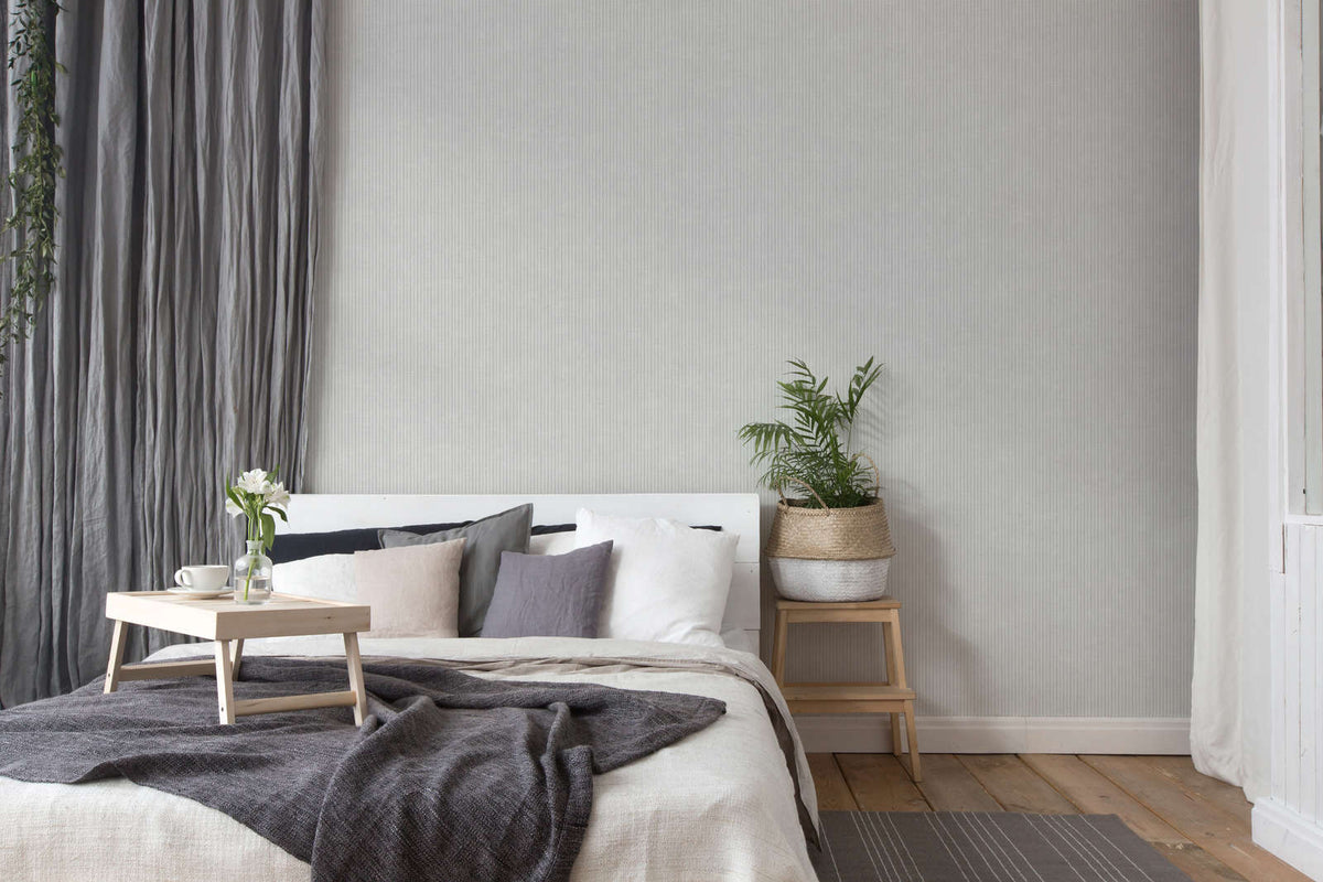 The Hushed Pinstripe | Mist Grey Luxe wallpaper hung behind a bed with charcoal and white bedding in a bedroom