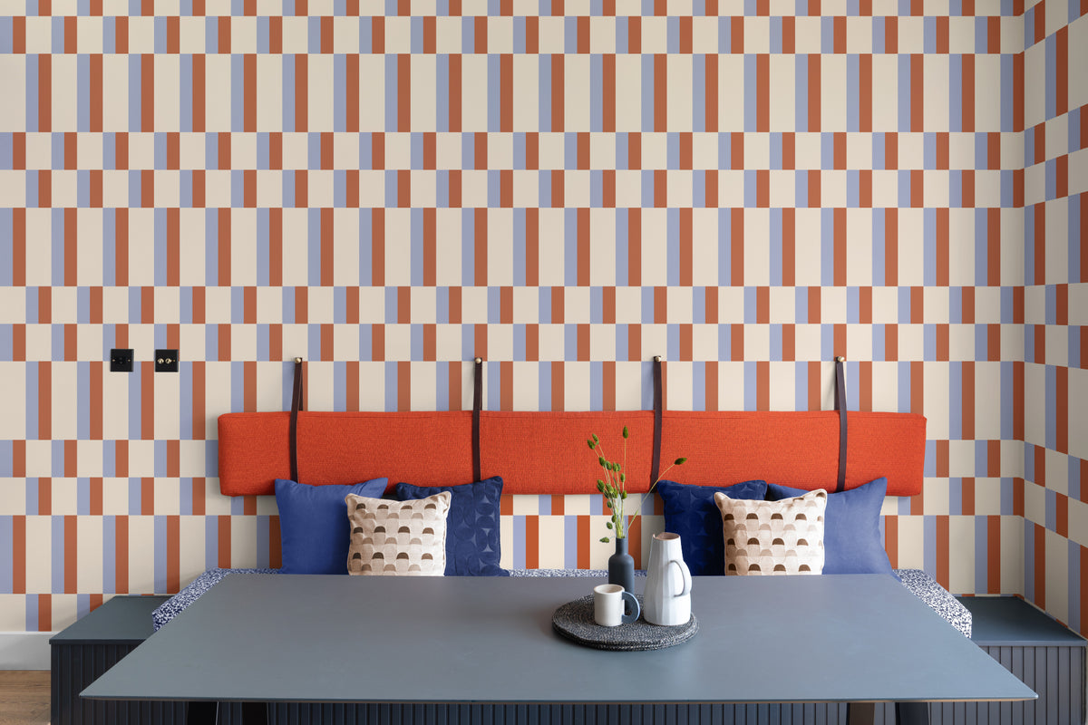 The Bauhaus Block wallpaper in periwinkle and rust behind the bed in a bedroom
