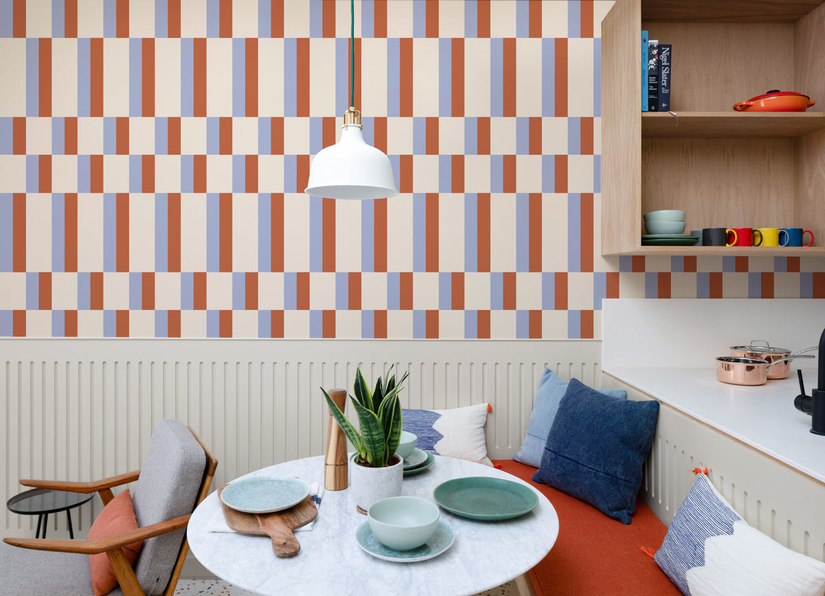 The Bauhaus Block wallpaper in periwinkle and rust behind a dining table