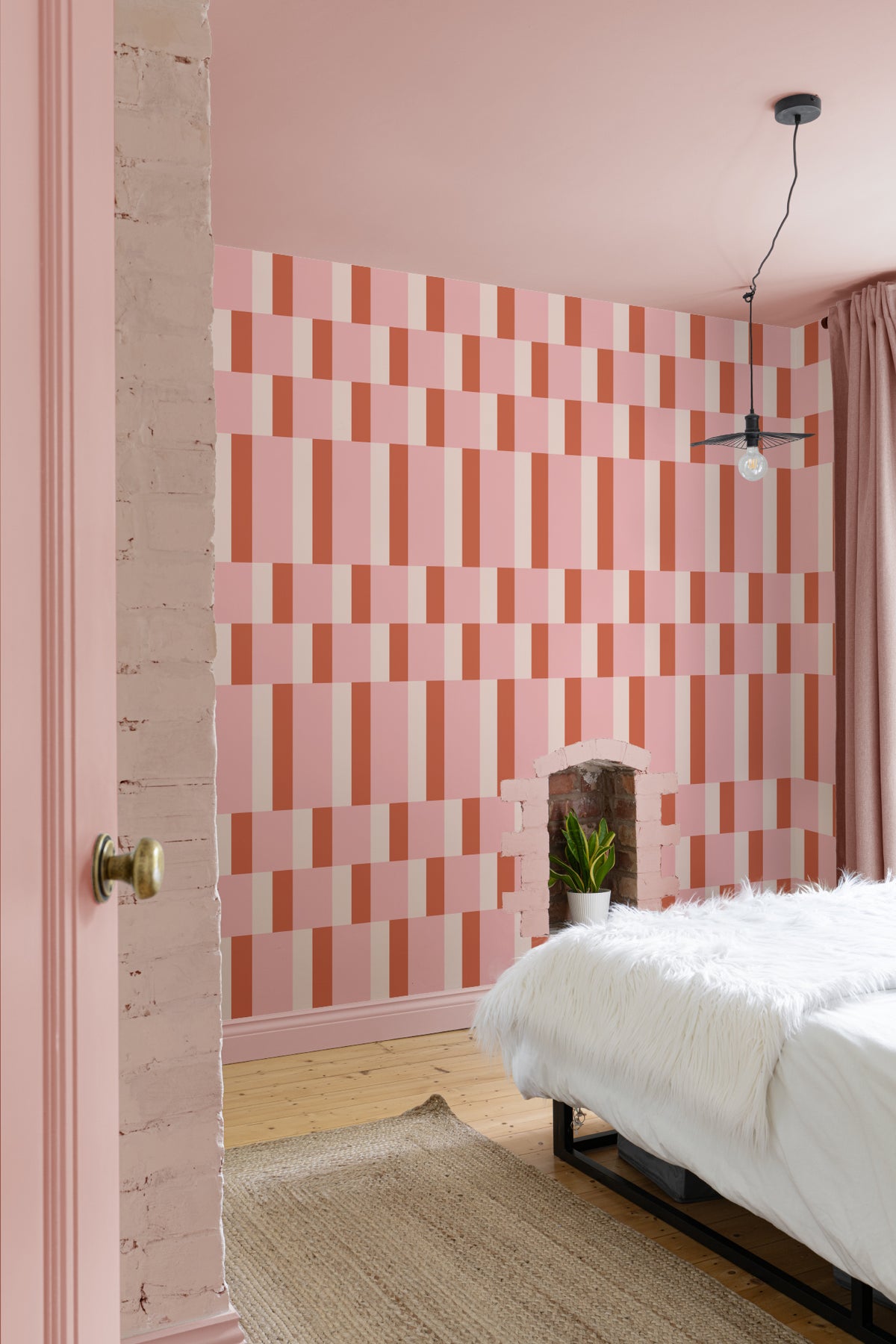 The Bauhaus Block wallpaper in rose and tangerine behind the bed in a bedroom
