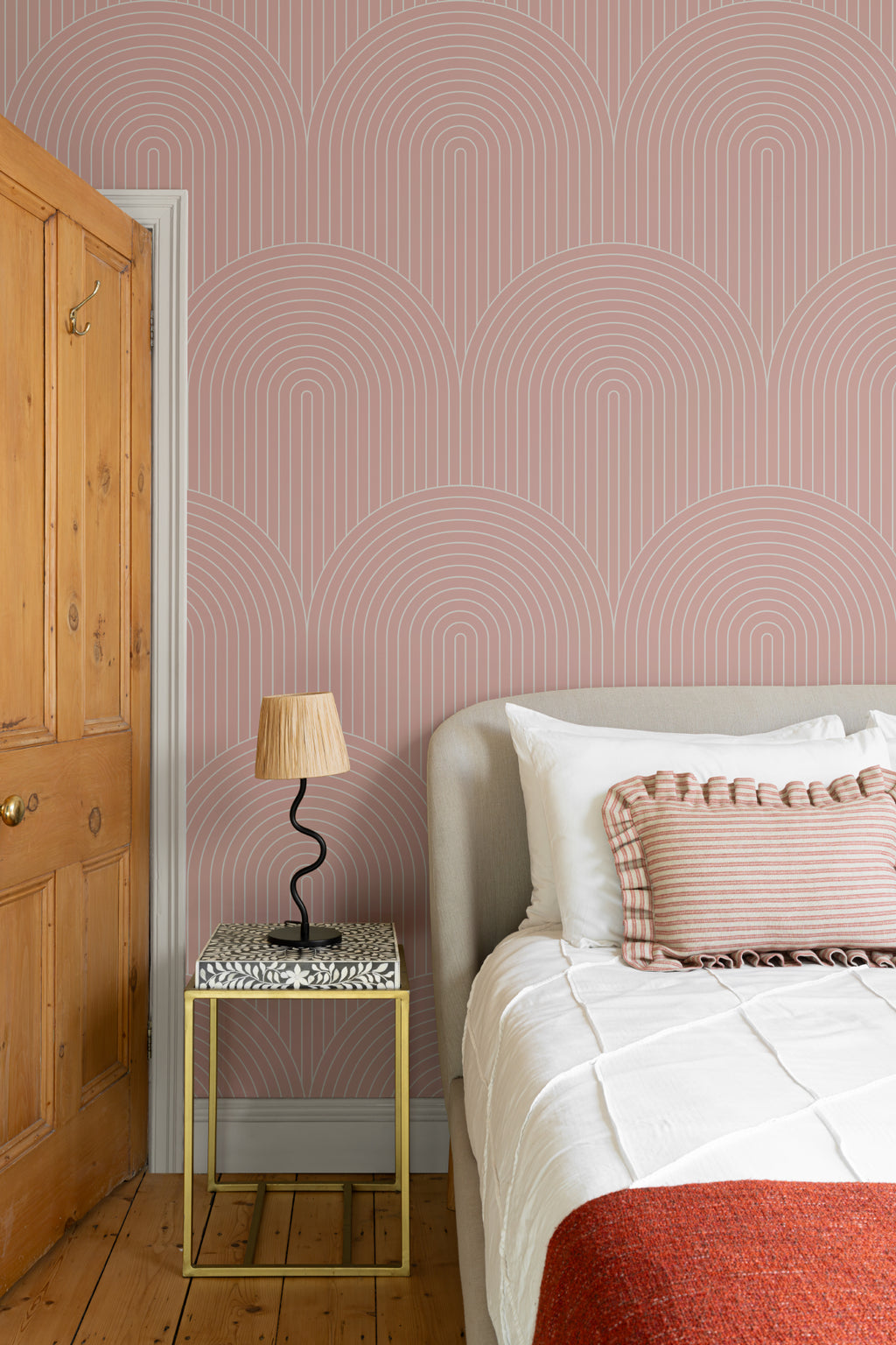The Deco Archway wallpaper in dusty rose behind the bed in a bedroom