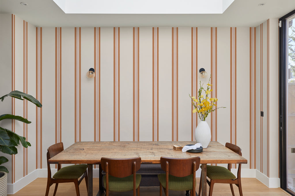 The Draughtsman Stripe wallpaper in burnt orange behind a dining table