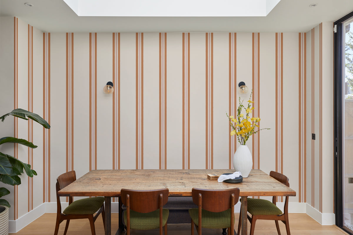 The Draughtsman Stripe wallpaper in burnt orange behind a dining table
