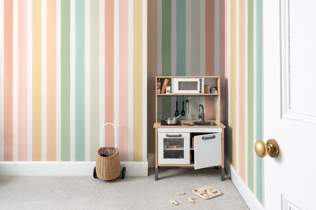 The Macaron Stripe mural in peach and mint behind a kids' play corner