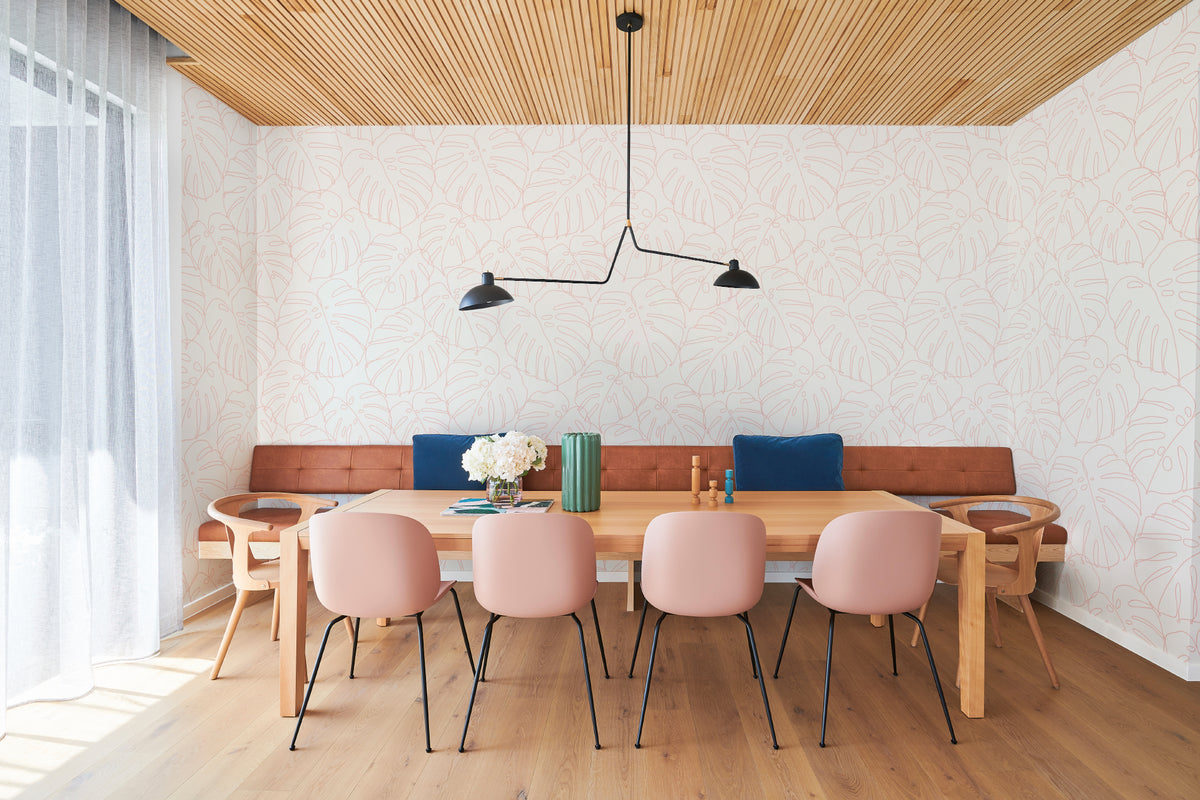 The Monstera Loggia wallpaper in blush and cream behind a dining table