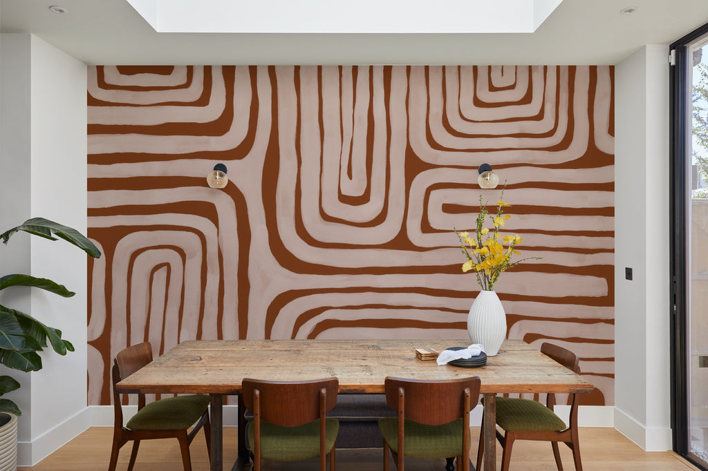 The Painted Labyrinth mural in terracotta and rose behind a dining table