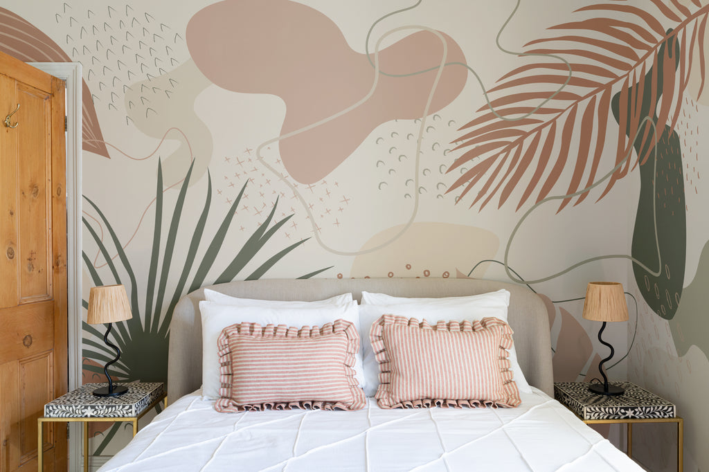 The Palm Cutout mural in clay pink and sage behind the bed in a bedroom