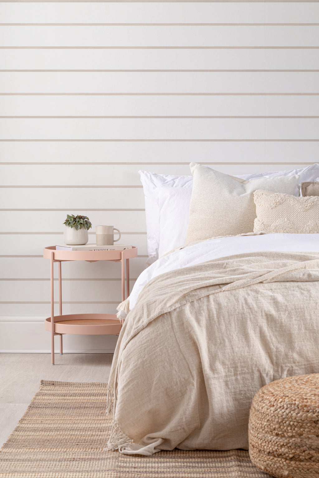 The Shoreline Stripe wallpaper in soft sand behind the bed in a bedroom