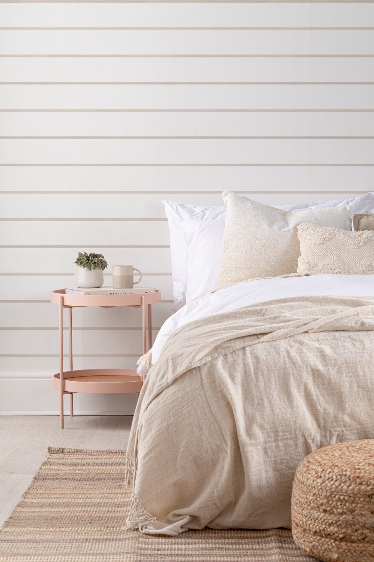 The Shoreline Stripe wallpaper in soft sand behind the bed in a bedroom