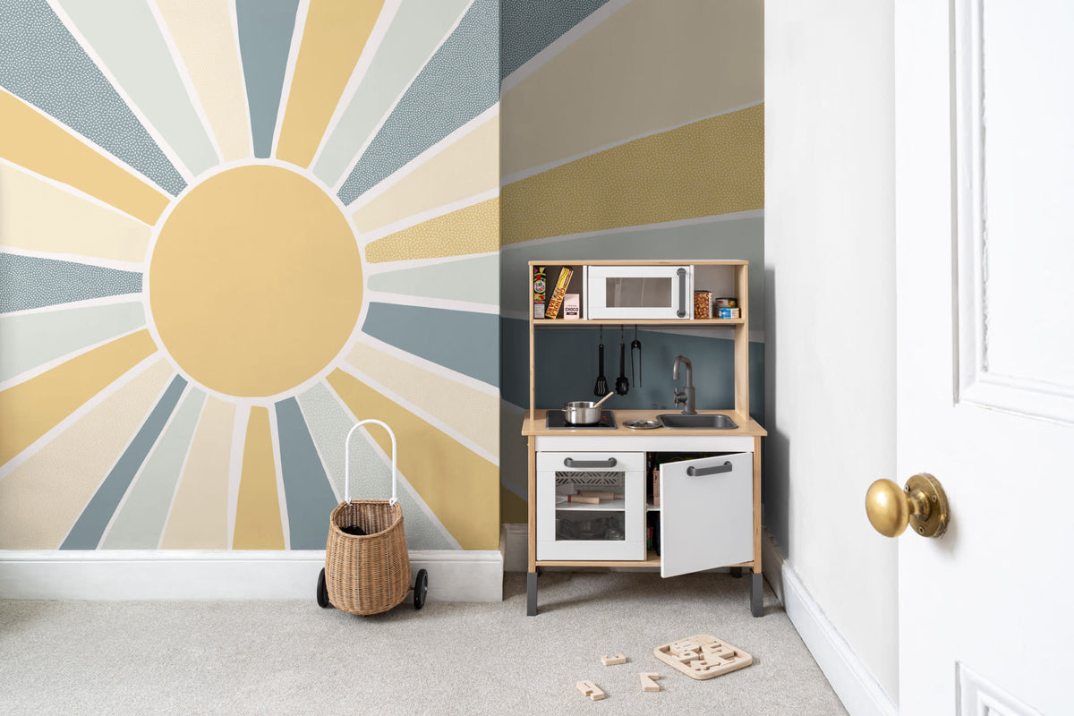 The Sunburst Morning mural in dusty blue and mustard behind a kids' play corner
